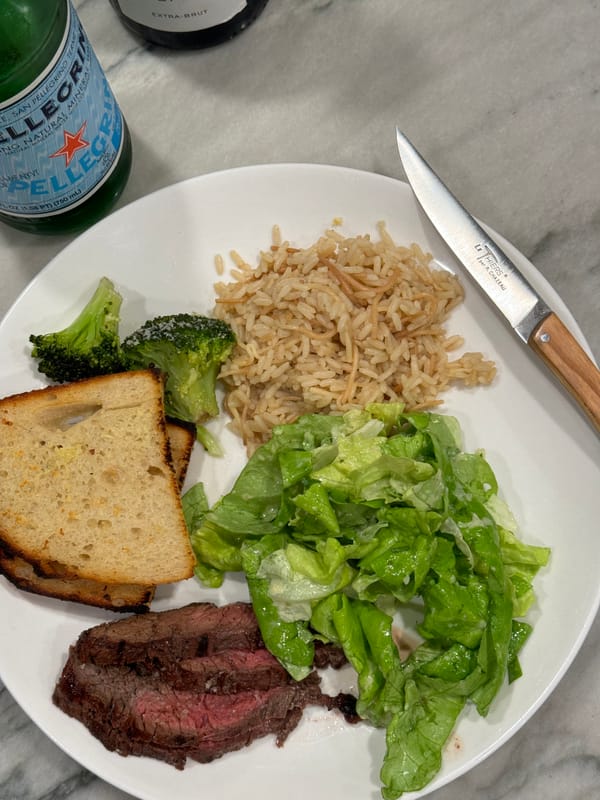 garlic bread, broccoli, pilaf, green salad and steak on a plate with a knife 